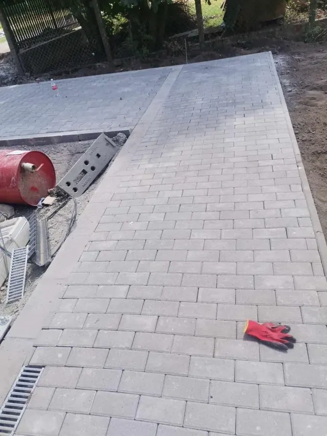 Világosszürke téglakő burkolat szegélykővel, mellette folyókaelemek beépítésre előkészítve