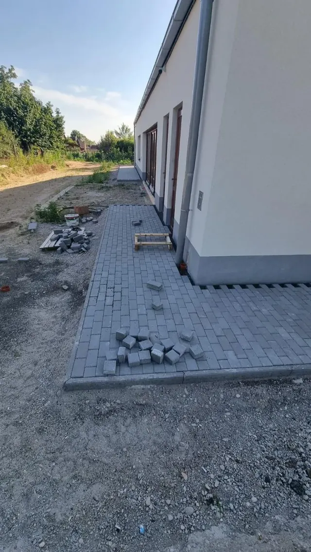Téglakő járda lerakása egy hosszú épület homlokzata mentén, szegéllyel