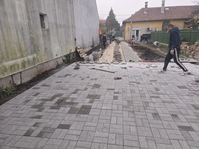 Szürke árnyalatos téglakő burkolat épület menti udvaron, a folytatás alapozásával